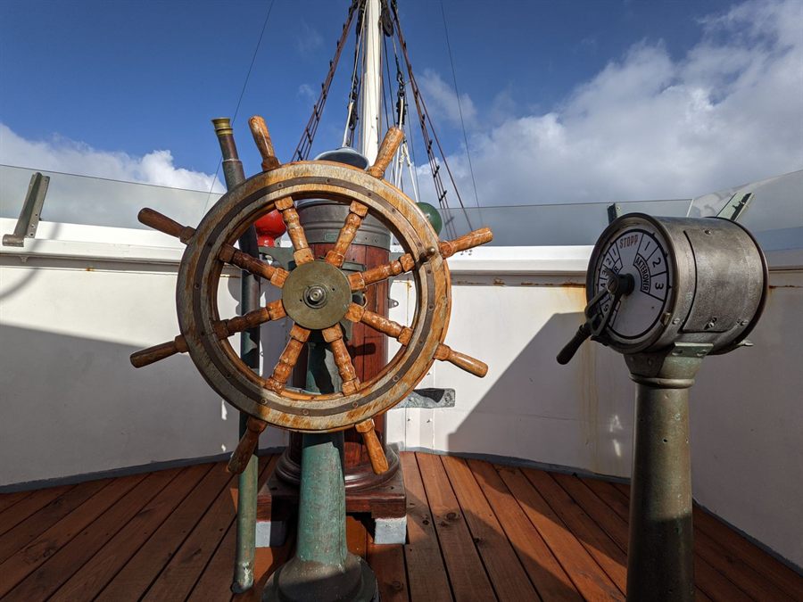Wooden ship&rsquo;s wheel and engine throttle against a blue sky