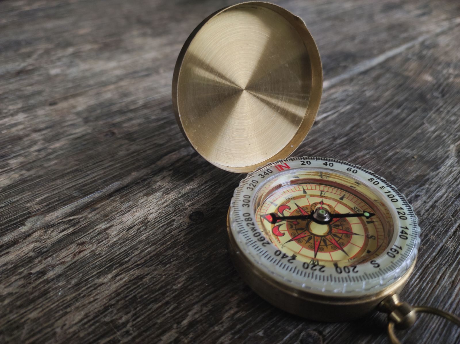 Open brass pocket compass on aged wood, a nautical collectible to examine for signs of reproduction
