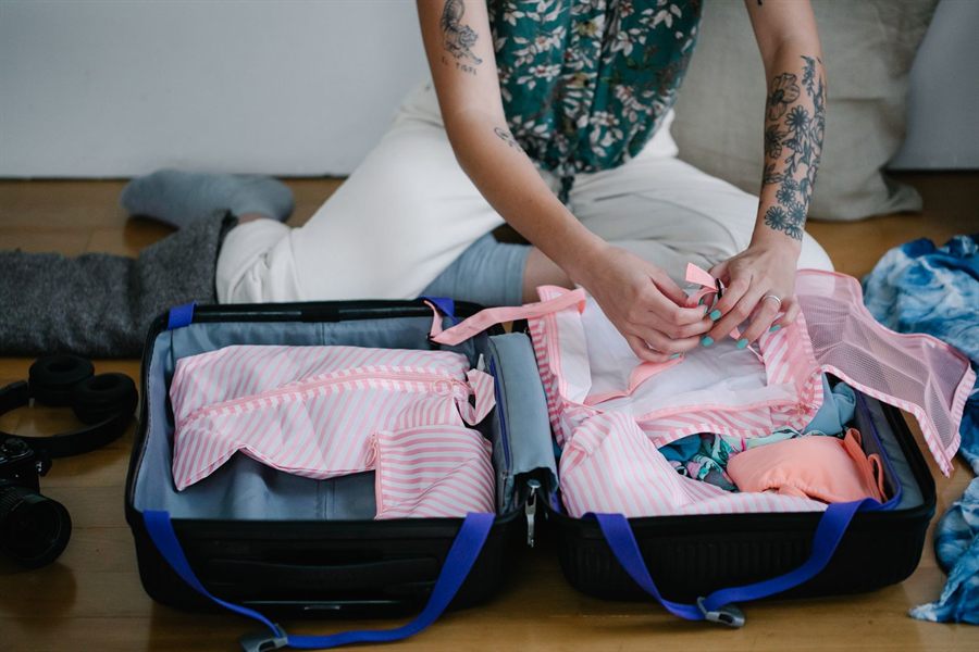 Traveler packing clothes into an open suitcase on the floor